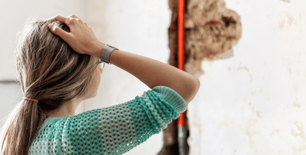 female with hand on head looking at a pipe in wall